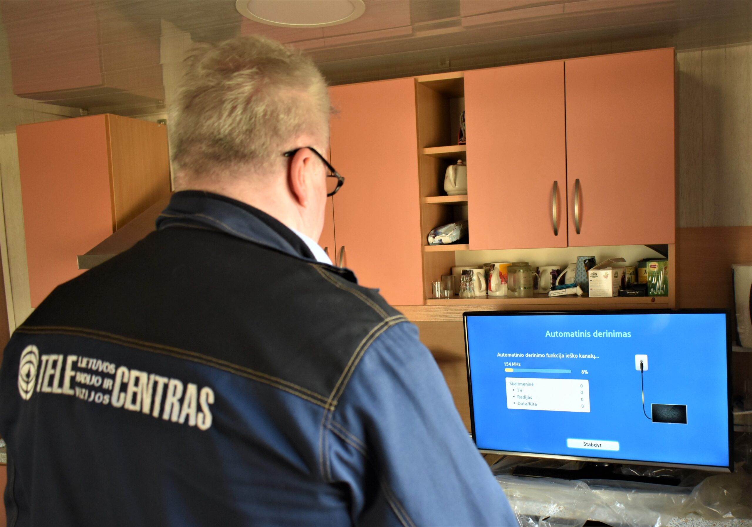 Telecentro specialistas prie televizoriaus skaito kanalus po antenos montavimo